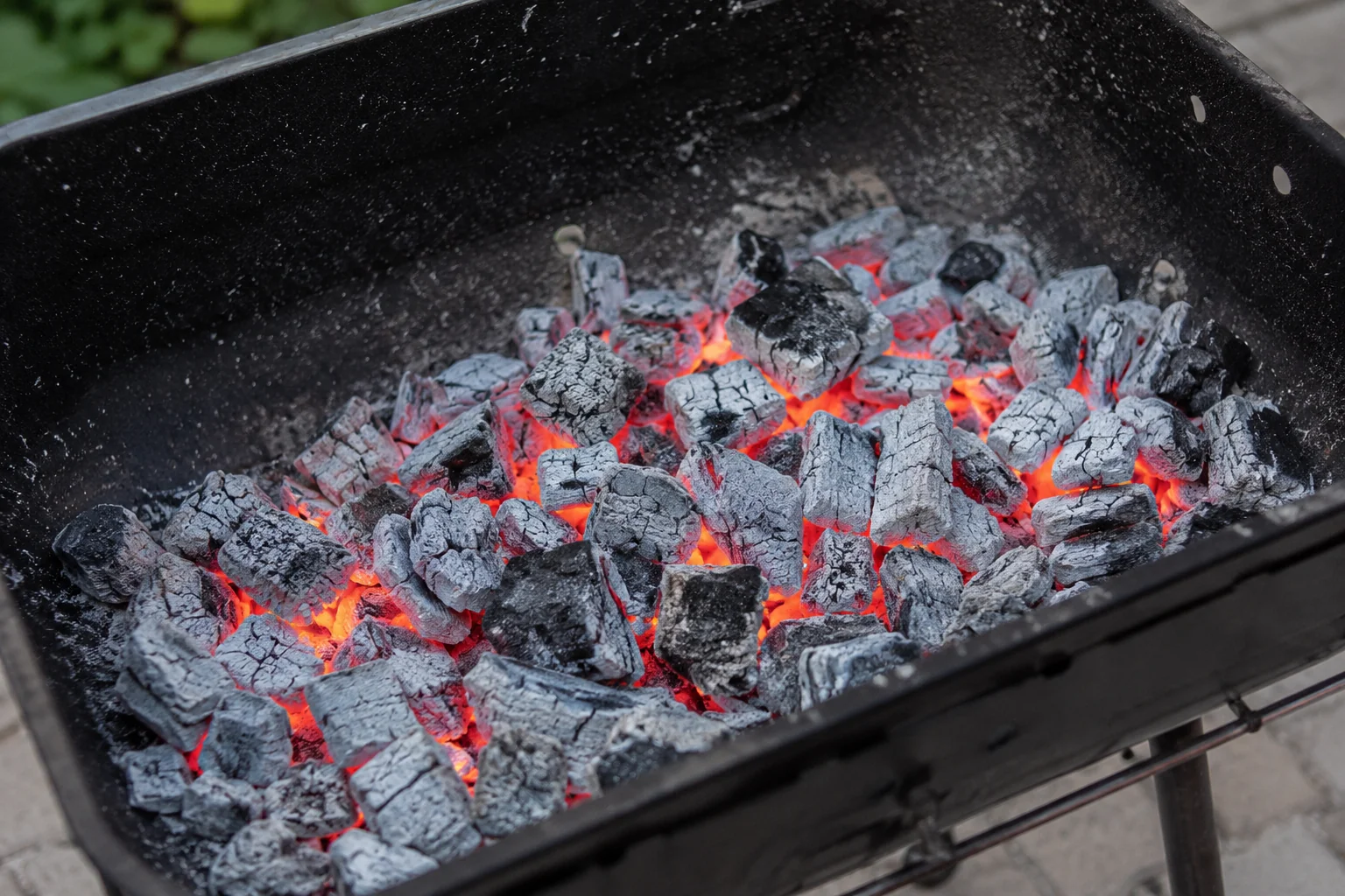 Brases roents en una barbacoa a punt per coure, amb petites flames entre el carbó