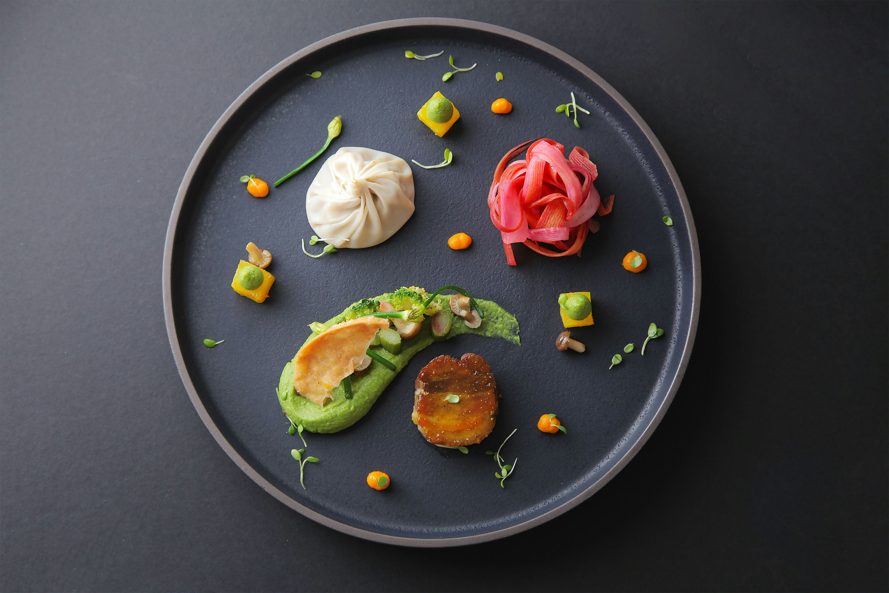 Plat d'alta cuina d'avantguarda amb elements vegetals i presentació artística sobre fons fosc