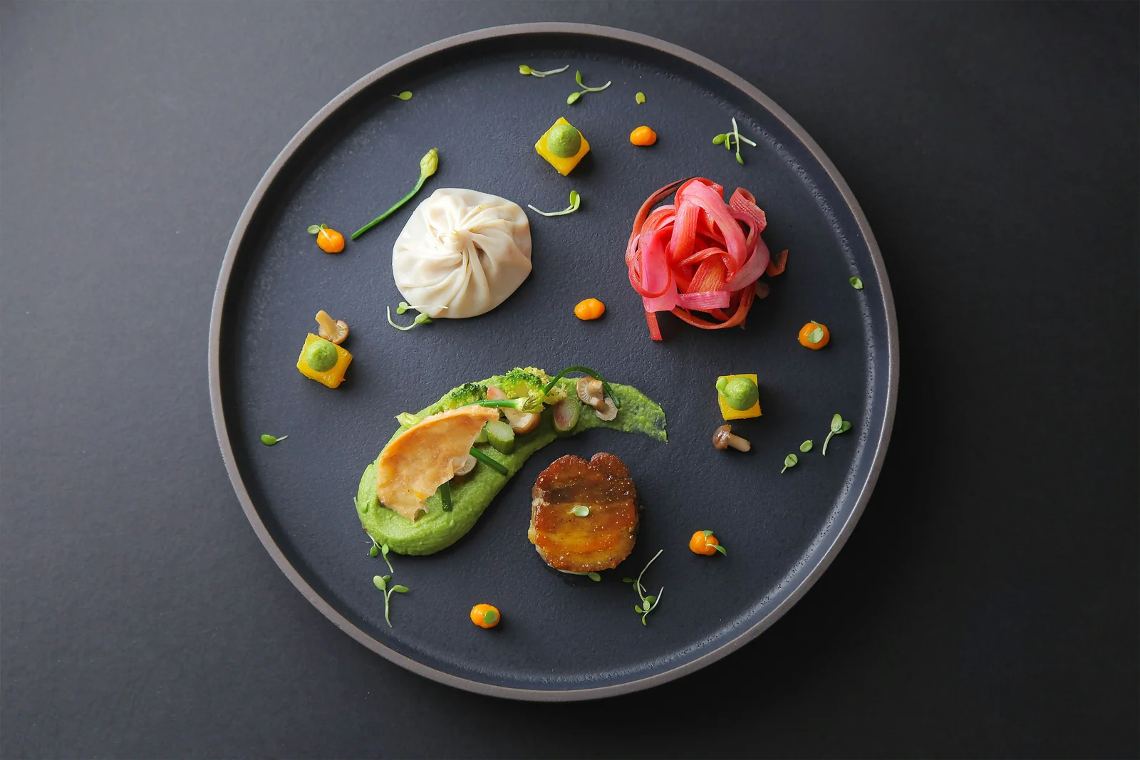 Plat d'alta cuina d'avantguarda amb elements vegetals i presentació artística sobre fons fosc
