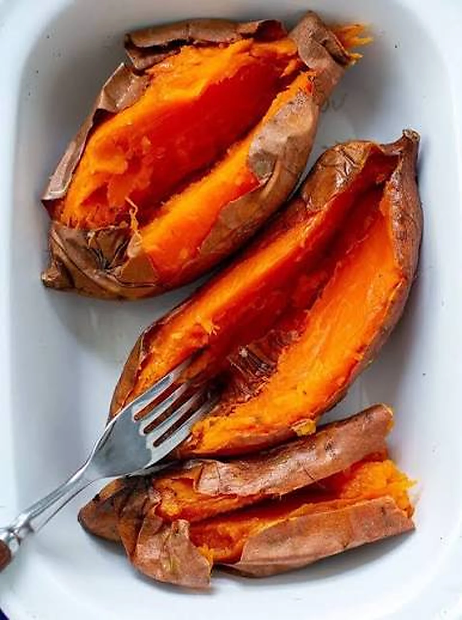 Moniatos al forn oberts per la meitat en una safata blanca, amb la pell arrugada i la carn taronja i tova